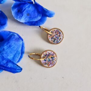 Orecchini cerchio in acciaio inossidabile con ciondolo in resina decorato con mix di fiori blu e viola su fondo bianco